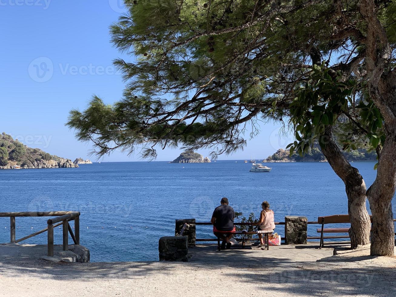 Summer landscape in Turkey near Marmaris. View of the bay and mountains through pine branches. Couple on the bench. photo