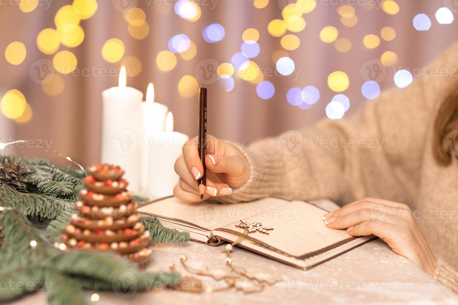 lista de deseos para el concepto de navidad de año nuevo escribiendo en el cuaderno. manos de mujer sosteniendo la pluma. planes de metas. fondo de color beige. plan para el próximo año foto