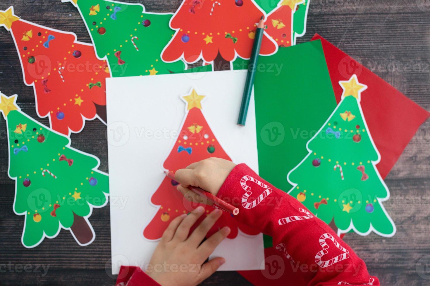niño dibuje y haga papel hecho a mano de navidad garaland árboles de navidad en mesa de madera. endecha plana manos de niño. foto