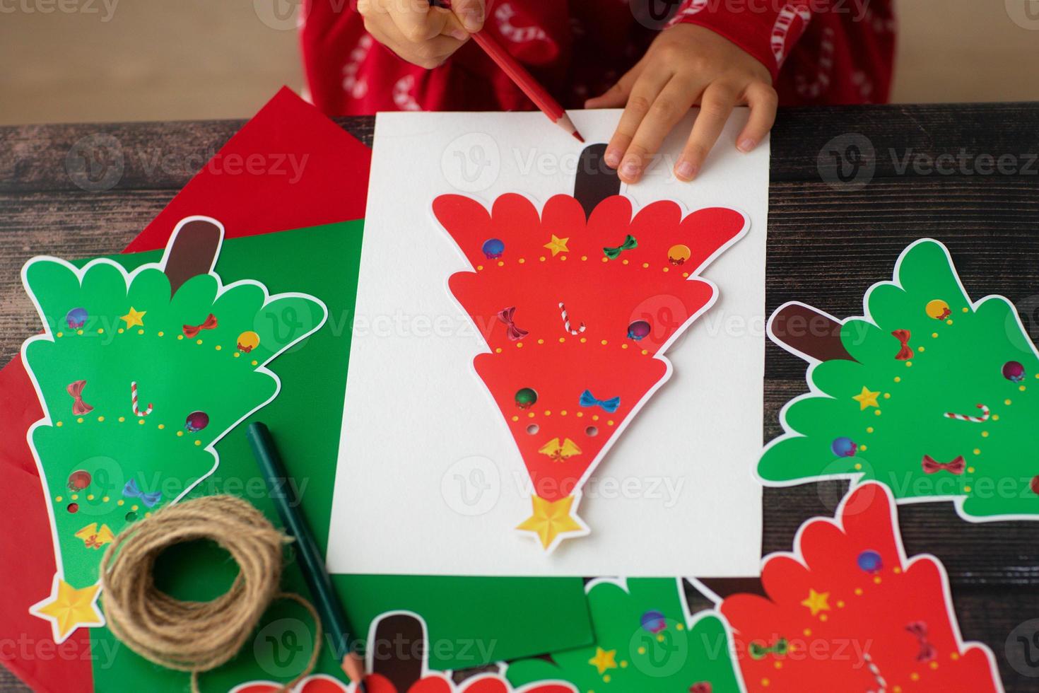 niño dibuje y haga papel hecho a mano de navidad garaland árboles de navidad en mesa de madera. endecha plana manos de niño. foto