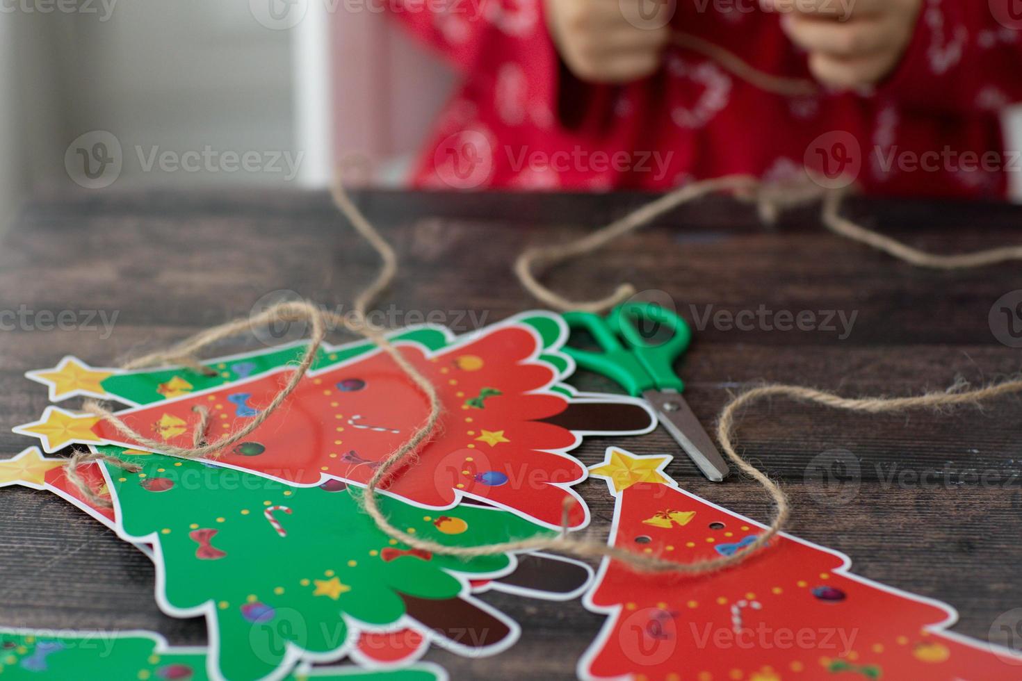 niño hacer navidad papel hecho a mano garaland árboles de navidad en mesa de madera. manos de niño. foto