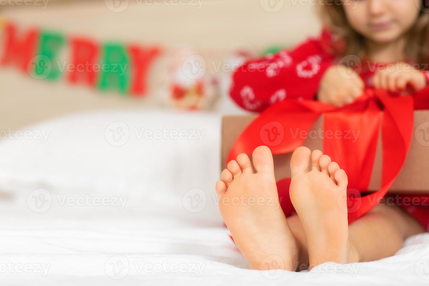 Children bare feet close up.Festive mood.Christmas concept, holiday.Happy New Year.Selective focus. Child girl sitting on bed holding open Christmas present.new Year's morning winter concept photo