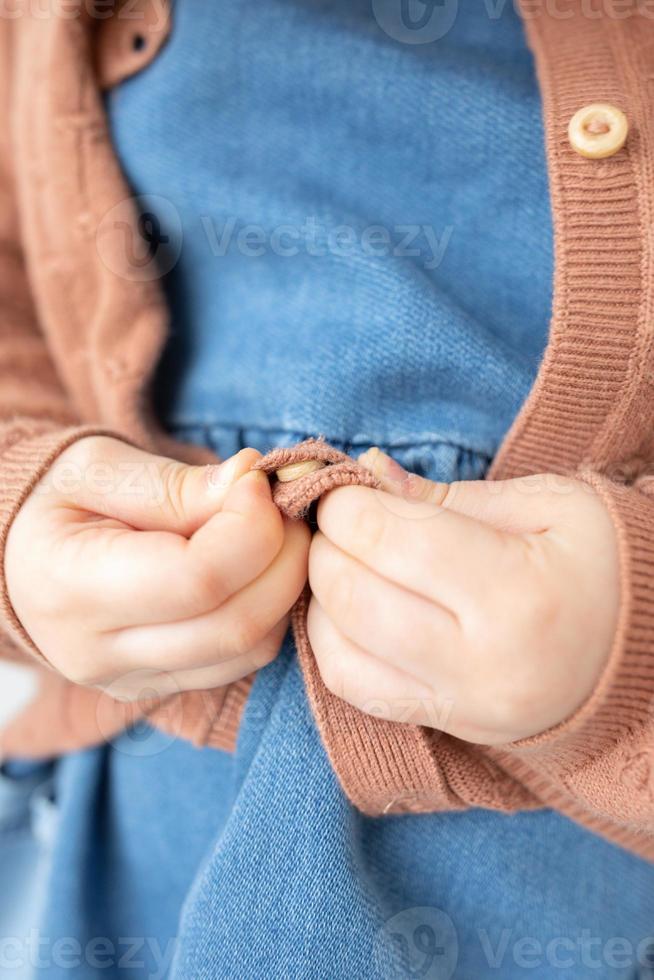 Child Development concept. Close up of little kindergarten kid hands learning to get dressed, buttoning blouse. Montessori practical life skills.Early Education. photo