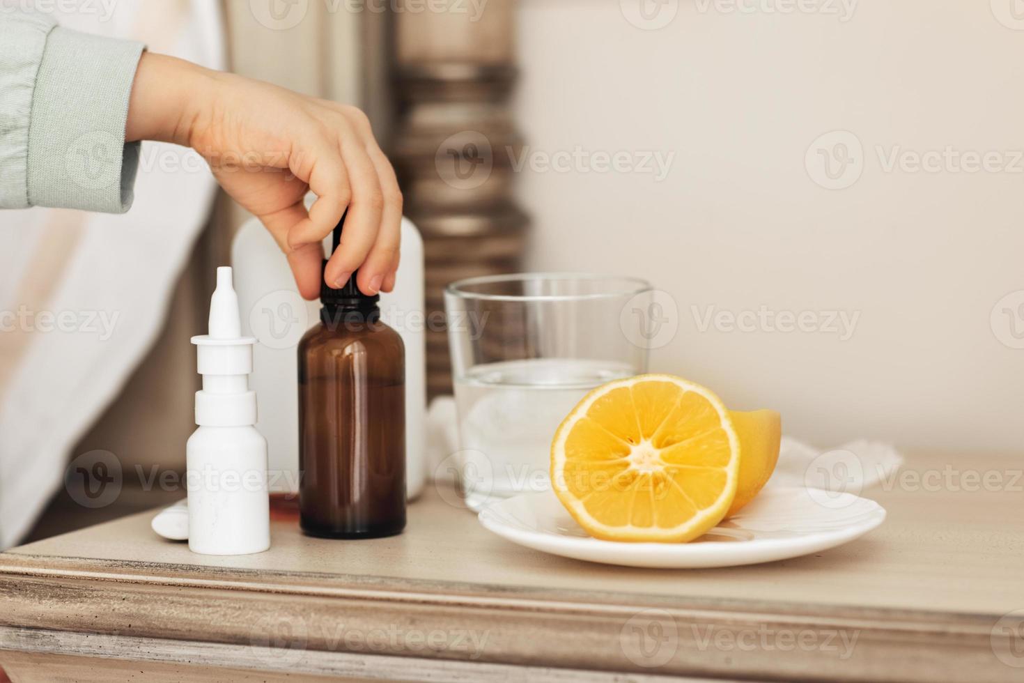 la mano del niño de primer plano toma el medicamento en una botella. medicamentos para la salud en la mesita de noche. gotas de botellas de maqueta y spray.niño enfermo en una cama foto