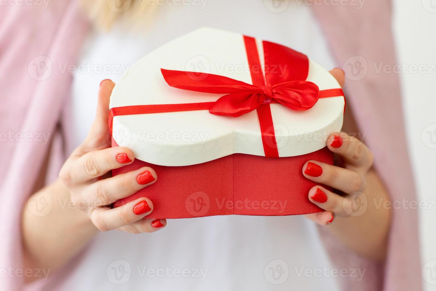 concepto de día de san valentín, vacaciones y regalo. cierre las manos de la mujer sostenga y abra la caja de regalo corazón rojo para el día de san valentín.entrega presente. sorpresa foto