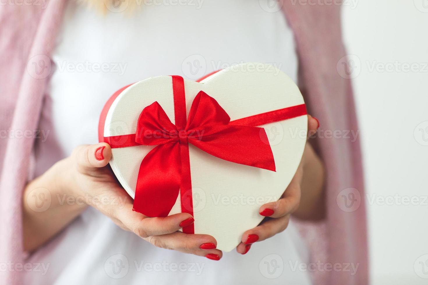 Valentine's day, holiday and gift concept. Close up hands of woman hold gift box red heart for Valentines Day.Delivery present. Surprise photo