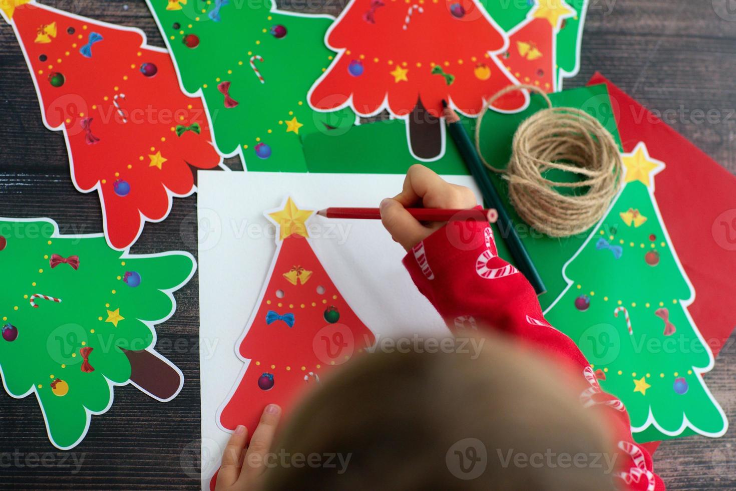 Child draw and make Christmas handmade paper garaland Christmas trees in wooden table. Flat lay. Kid hands. photo