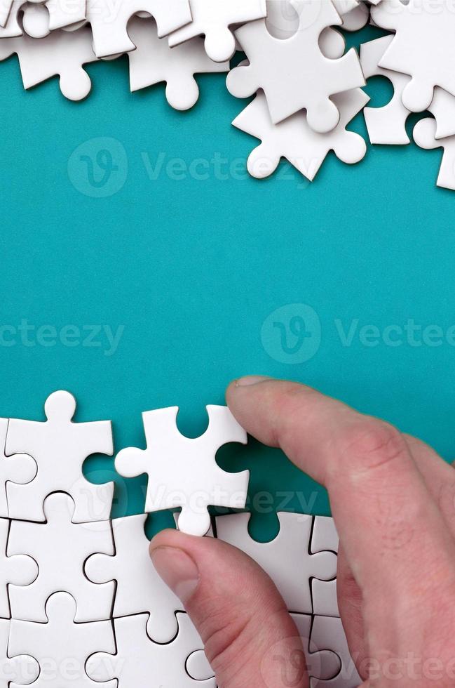 The hand folds a white jigsaw puzzle and a pile of uncombed puzzle pieces lies against the background of the blue surface. Texture photo with space for text