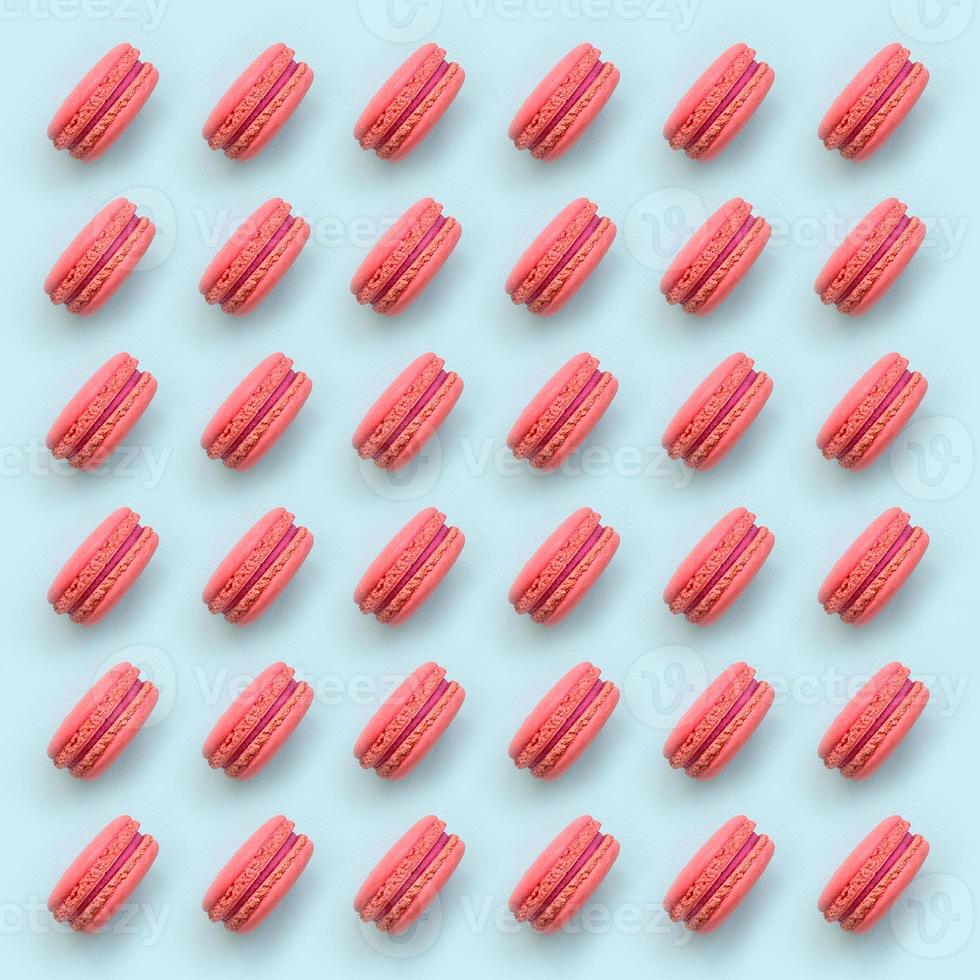 Pink dessert cake macaron or macaroon on trendy pastel blue background top view. Flat lay pattern composition photo