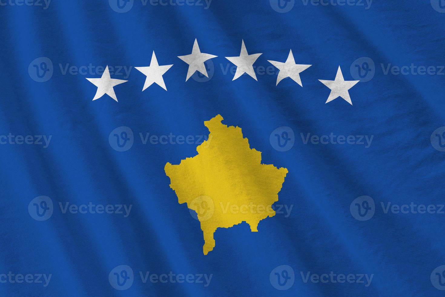 Kosovo flag with big folds waving close up under the studio light indoors. The official symbols and colors in banner photo