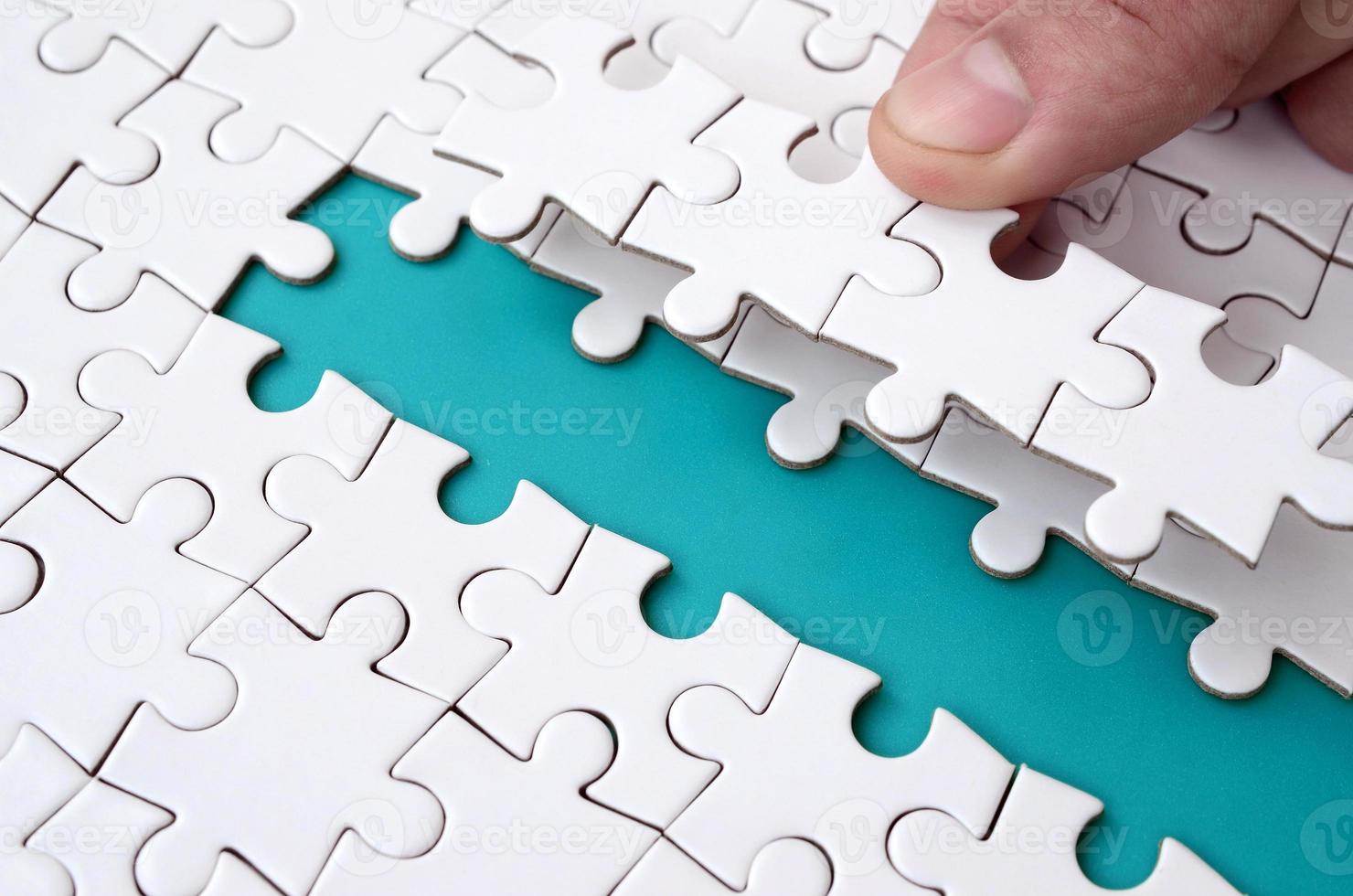 The human hand paves the way to the surface of the jigsaw puzzle, forming a blue space. The concept of overcoming the difficulties on the way to success photo