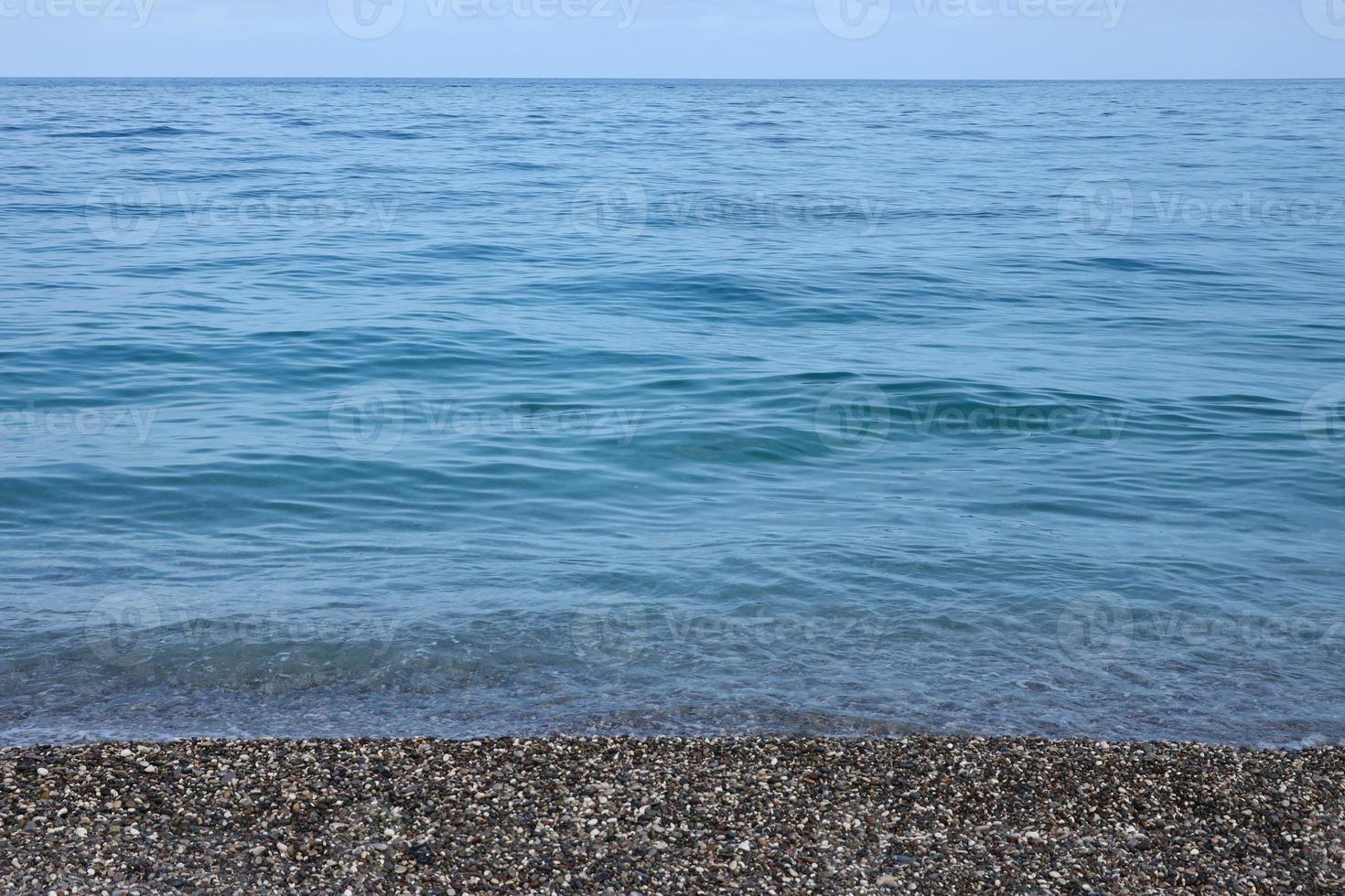 Bank of pebbles with the sea and beach in the background photo