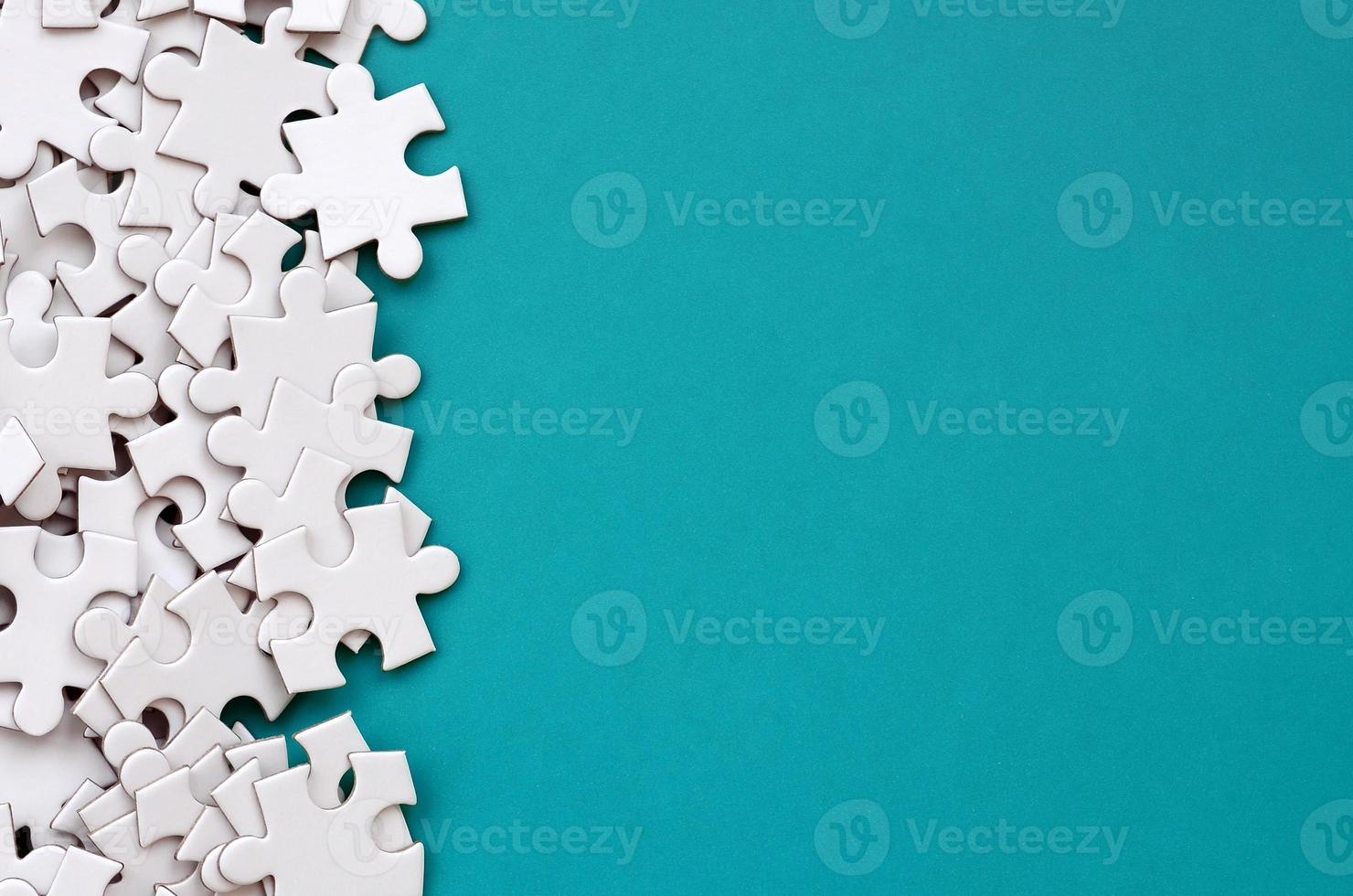 A pile of uncombed elements of a white jigsaw puzzle lies on the background of a blue surface. Texture photo with copy space for text