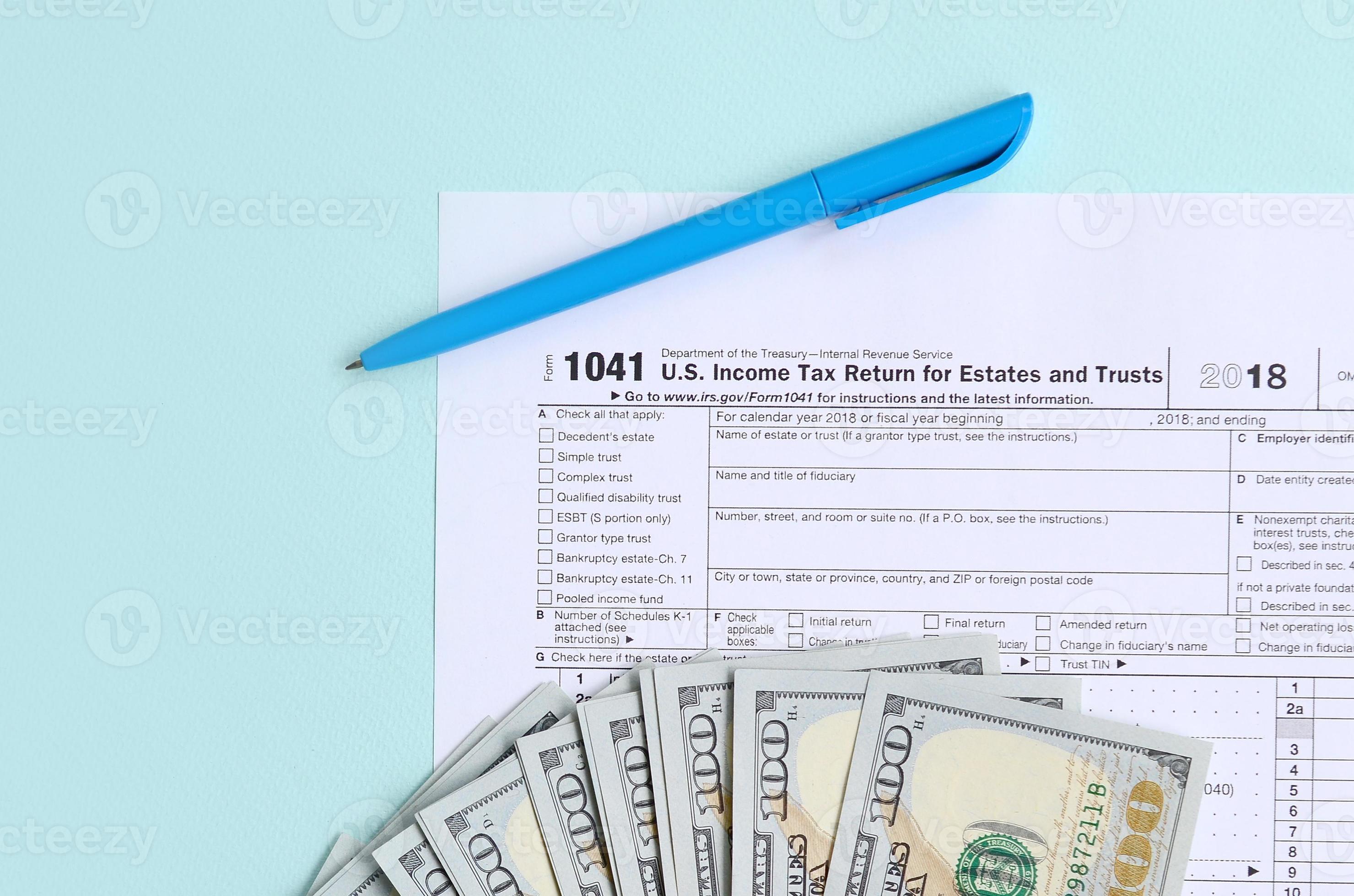 1041 tax form lies near hundred dollar bills and blue pen on a light