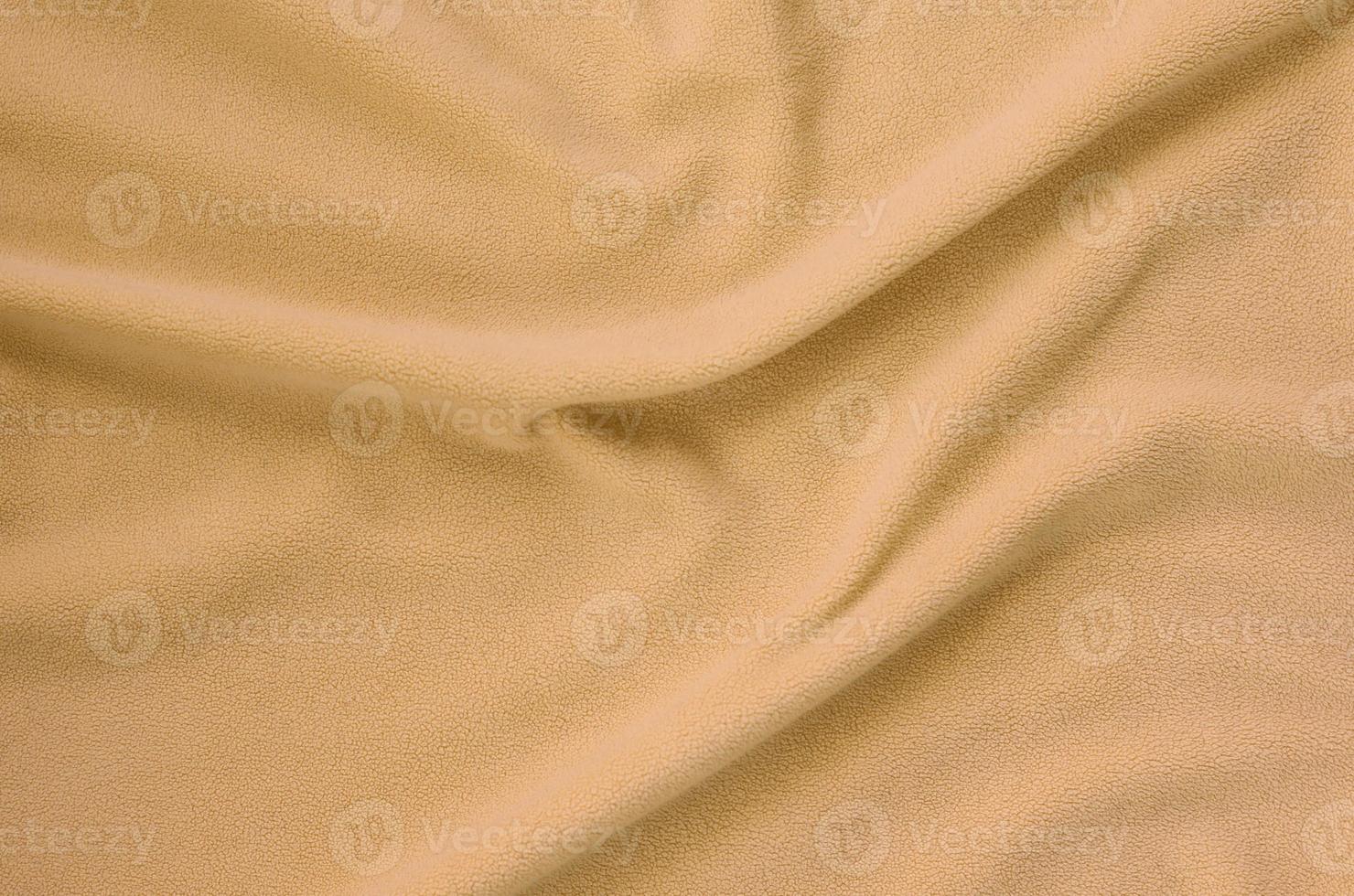 The blanket of furry orange fleece fabric. A background of light orange soft plush fleece material with a lot of relief folds photo