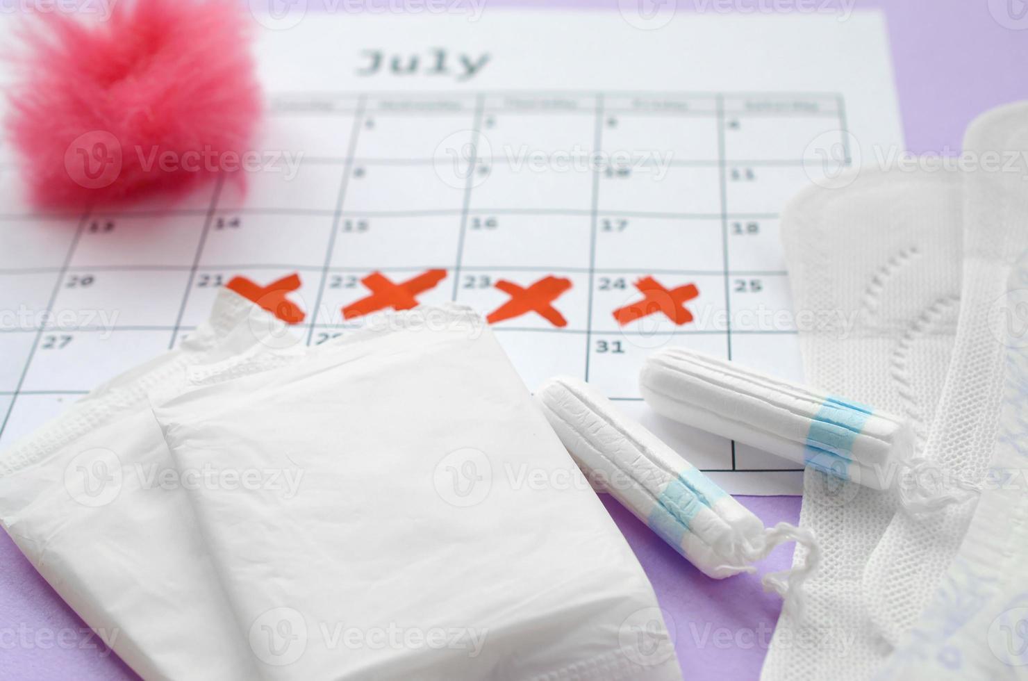 almohadillas menstruales y tampones en el calendario del período de menstruación con marcas de cruz roja sobre fondo lila foto