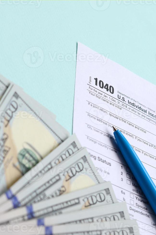1040 tax form lies near hundred dollar bills and blue pen on a light blue background. US Individual income tax return photo