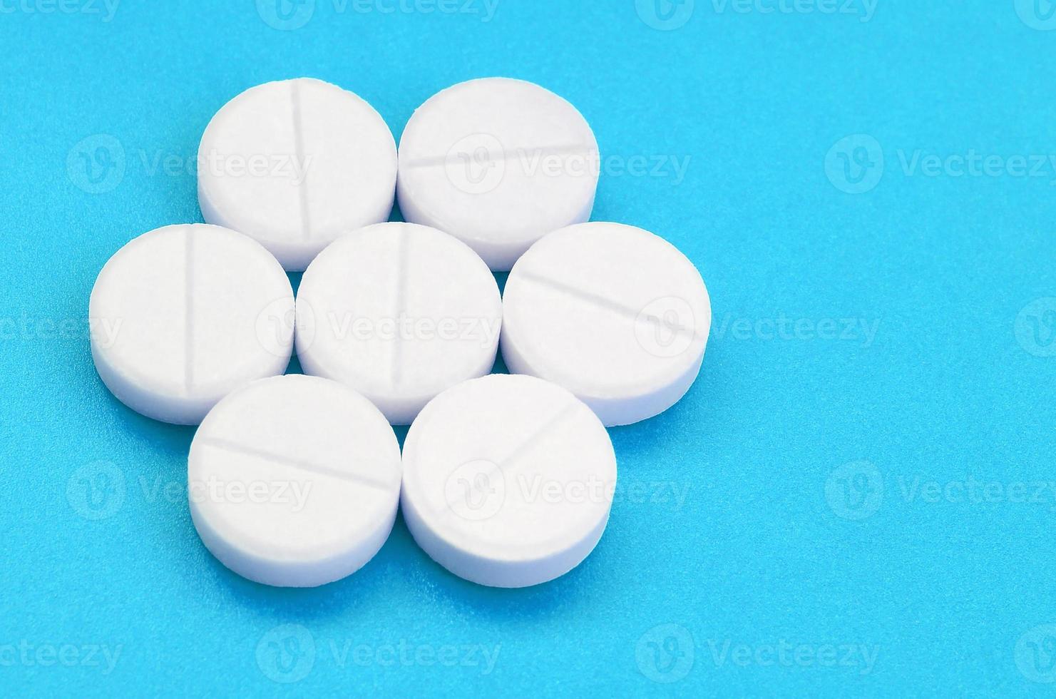 A few white tablets lie on a bright blue background surface. Background image on medical and pharmaceutical topics photo