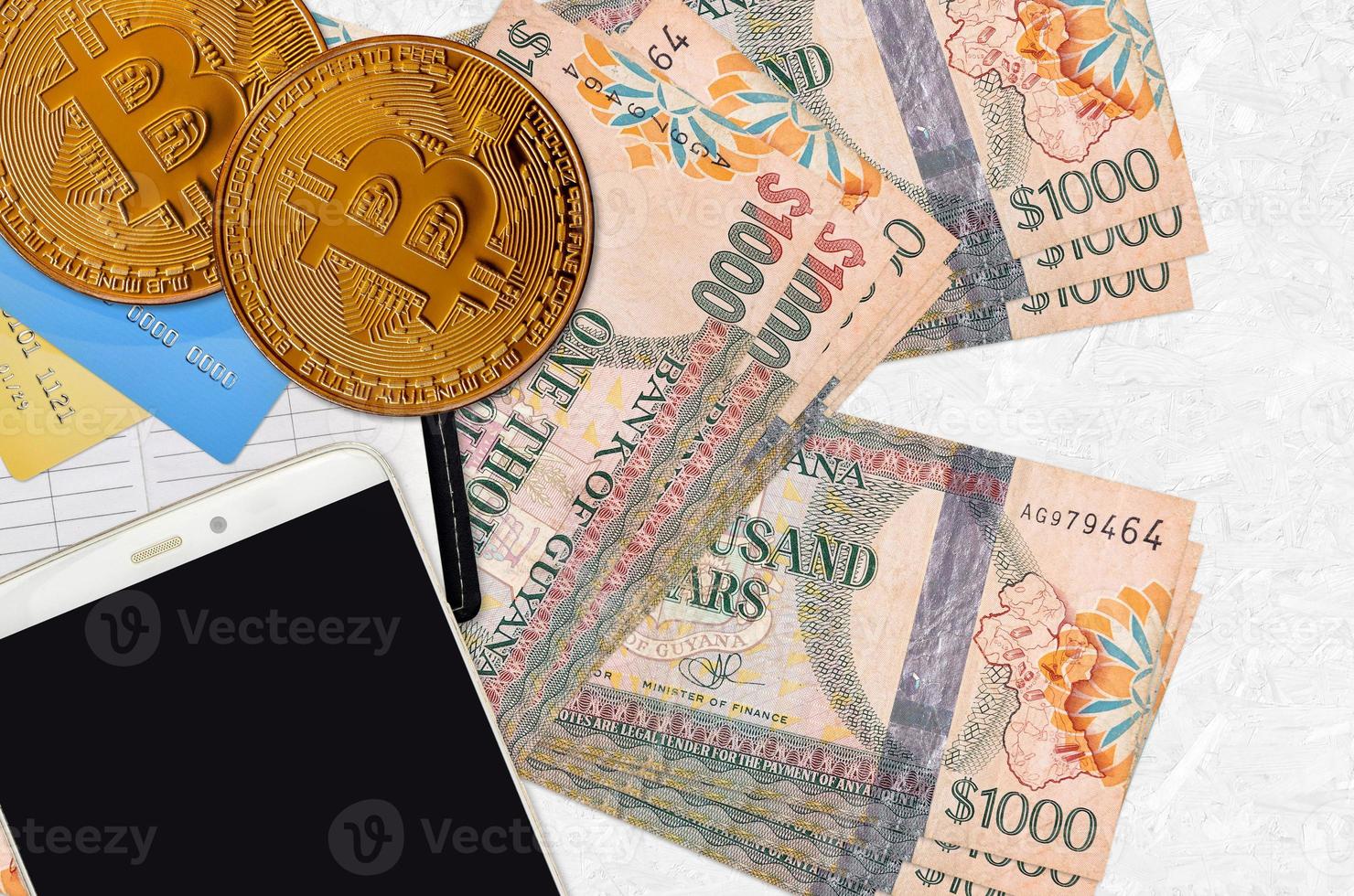 1000 Guyanese dollars bills and golden bitcoins with smartphone and credit cards. Cryptocurrency investment concept. Crypto mining or trading photo
