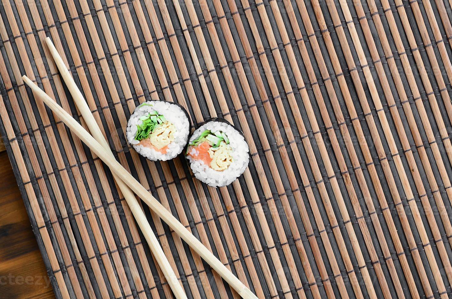Sushi rolls and wooden chopsticks lie on a bamboo straw serwing mat. Traditional Asian food. Top view. Flat lay minimalism shot with copy space photo