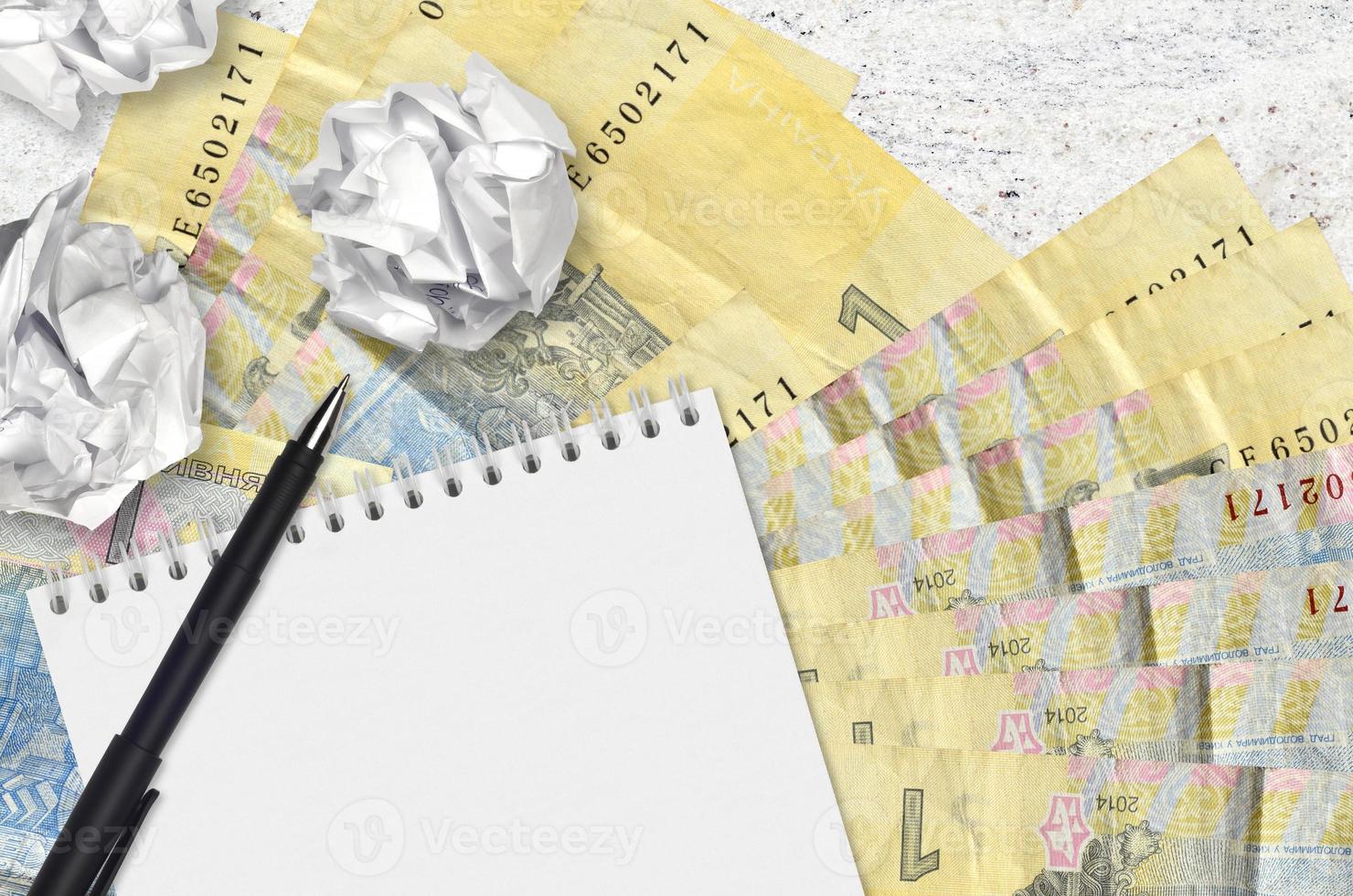 1 Ukrainian hryvnia bills and balls of crumpled paper with blank notepad. Bad ideas or less of inspiration concept. Searching ideas for investment photo