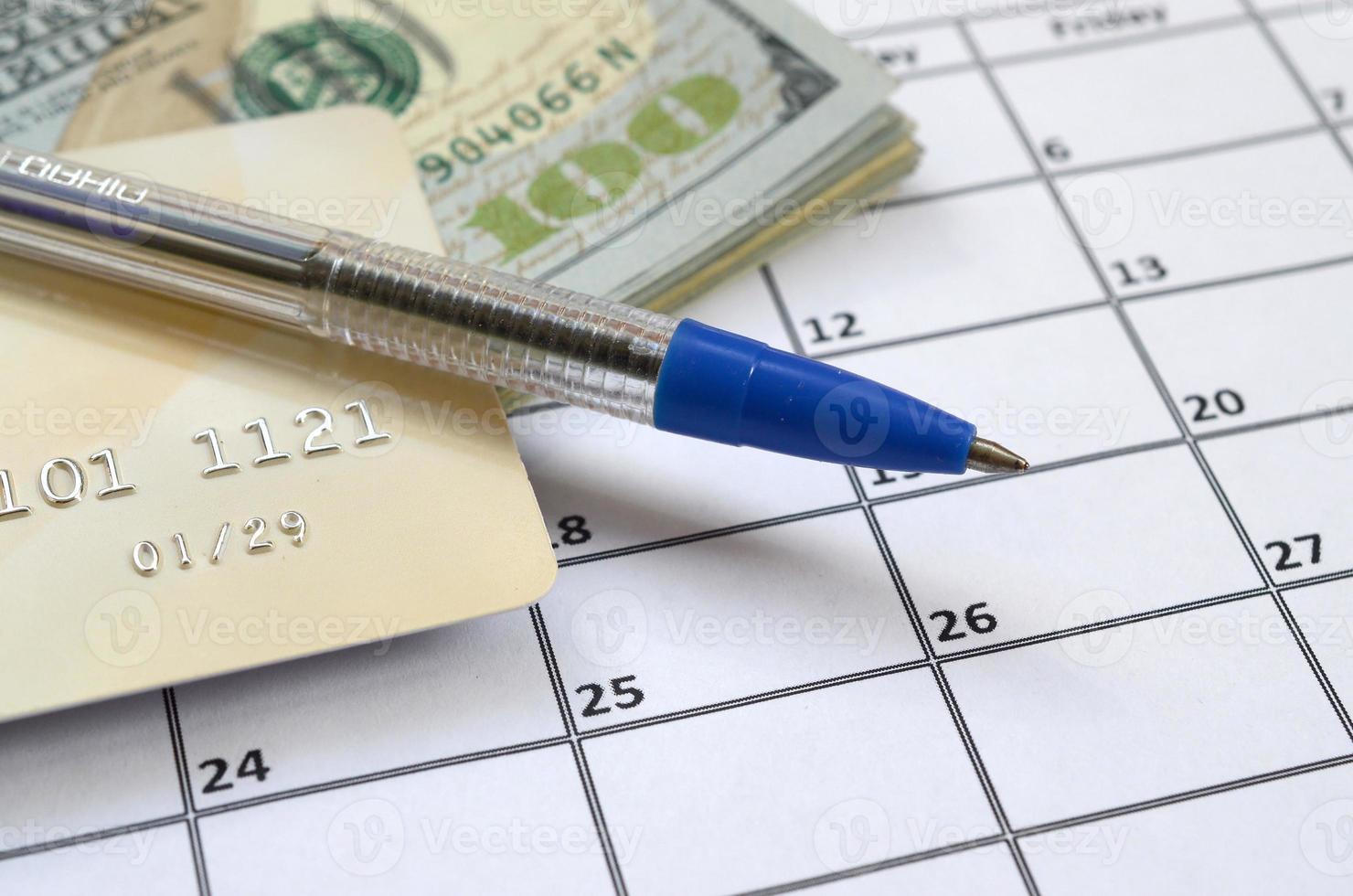Pen and credit card on many hundred US dollar bills on calendar page close up photo