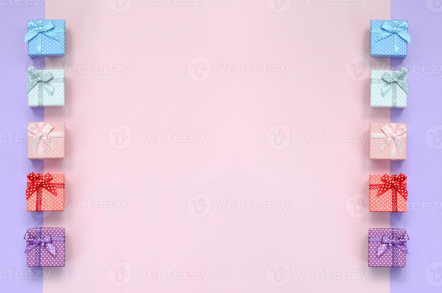 Small gift boxes of different colors with ribbons lies on a violet and pink color background photo