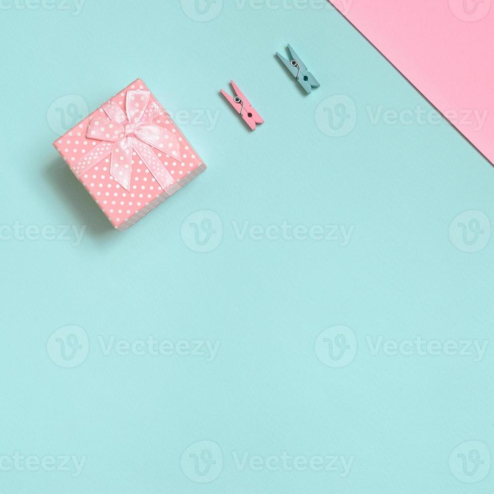 Small pink gift box and two pegs lie on texture background of fashion pastel blue and pink colors paper in minimal concept photo