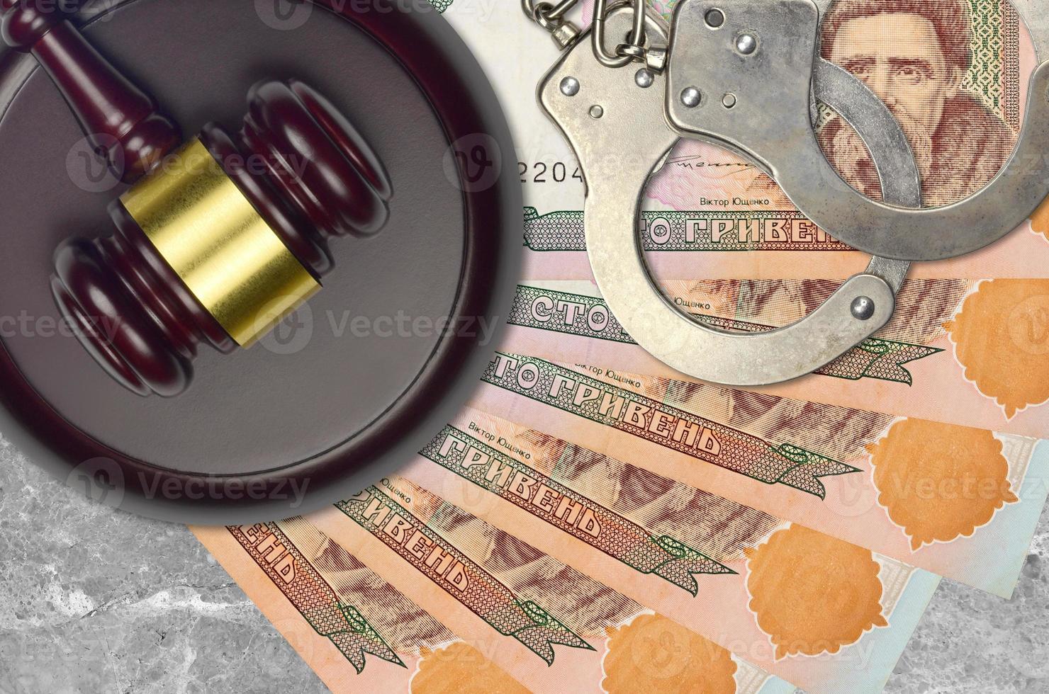 100 Ukrainian hryvnias bills and judge hammer with police handcuffs on court desk. Concept of judicial trial or bribery. Tax avoidance photo