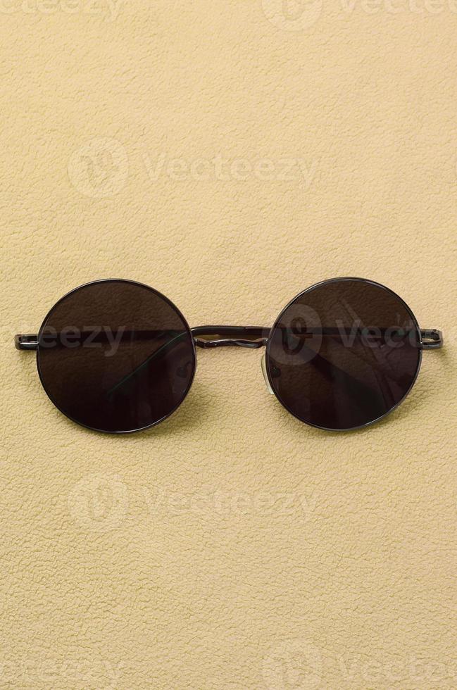 elegantes gafas de sol negras con gafas redondas se encuentran sobre una manta hecha de suave y esponjosa tela de lana naranja claro. imagen de fondo de moda en colores de moda foto