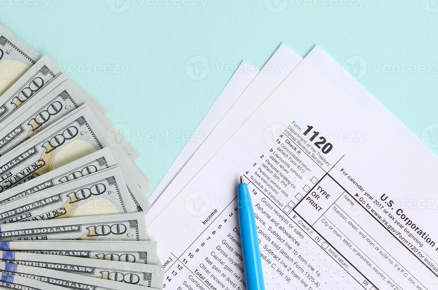 El formulario de impuestos 1120 se encuentra cerca de los billetes de cien dólares y el bolígrafo azul sobre un fondo azul claro. declaración de impuestos sobre la renta de la corporación estadounidense foto