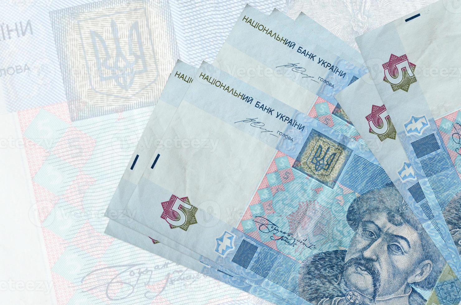 5 Ukrainian hryvnias bills lies in stack on background of big semi-transparent banknote. Abstract presentation of national currency photo