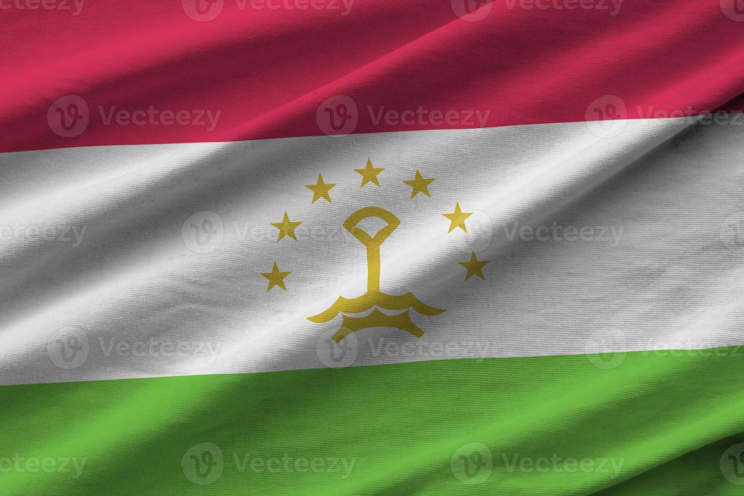 Tajikistan flag with big folds waving close up under the studio light indoors. The official symbols and colors in banner photo