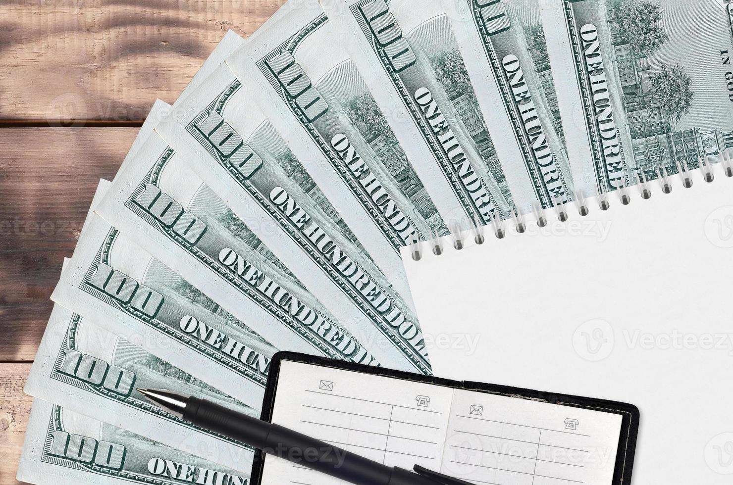 Ventilador de billetes de 100 dólares estadounidenses y bloc de notas con libreta de contactos y bolígrafo negro. concepto de planificación financiera y estrategia empresarial foto
