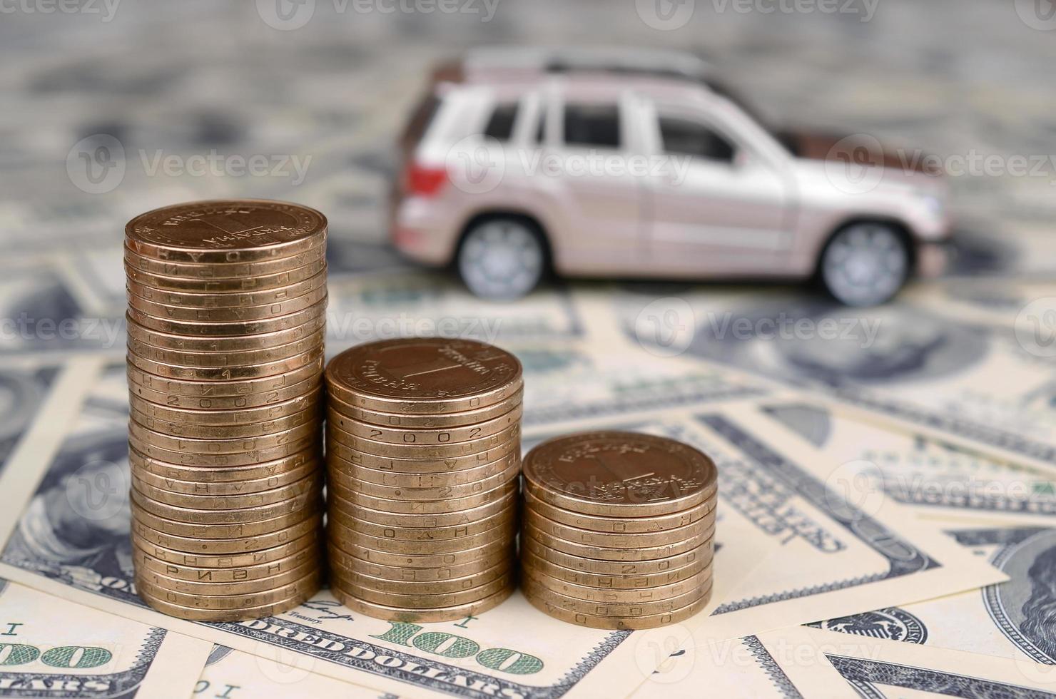 Toy car model at the stacks of golden coins lies on many dollar bills photo