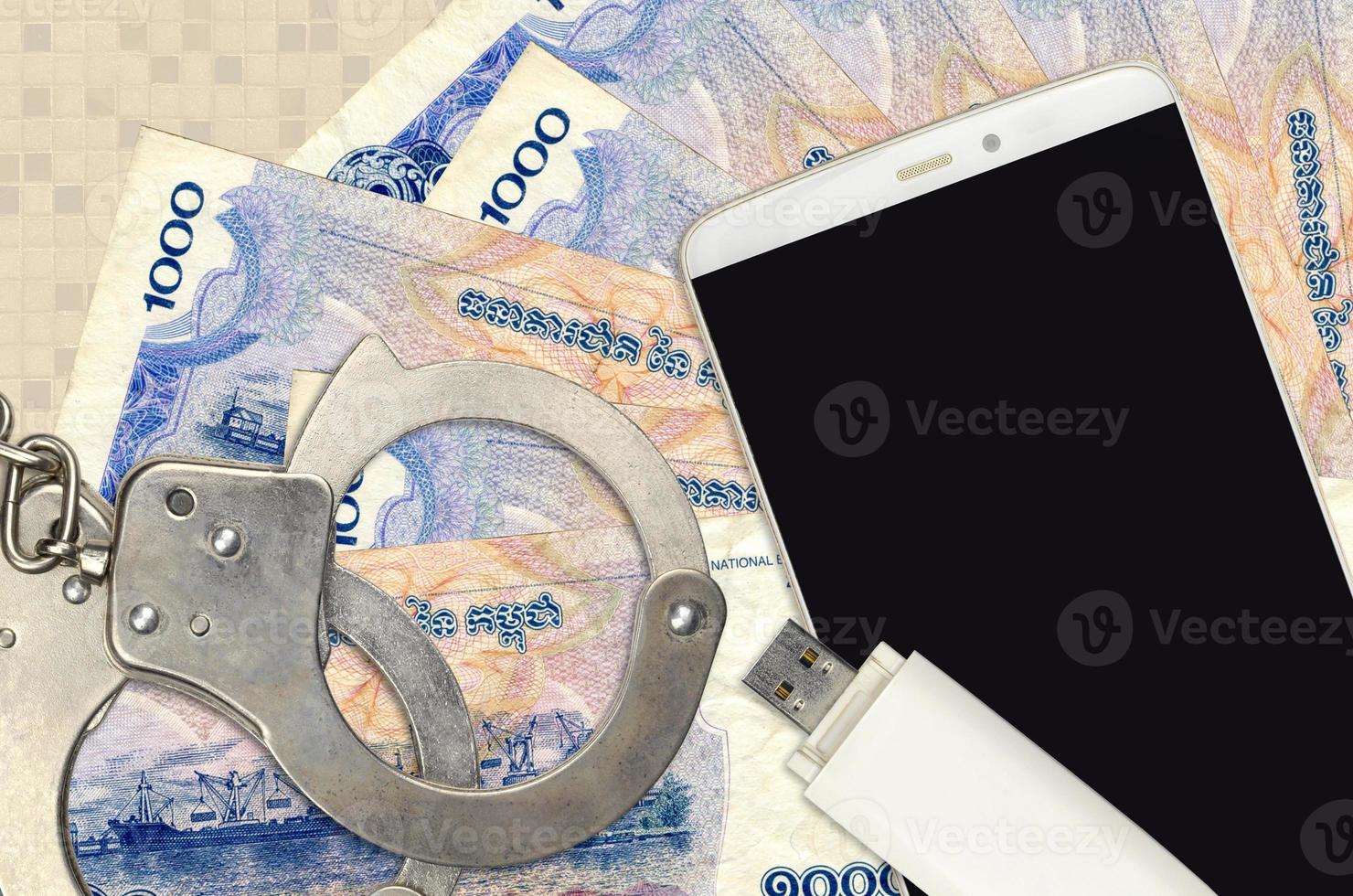 1000 Cambodian riels bills and smartphone with police handcuffs. Concept of hackers phishing attacks, illegal scam or malware soft distribution photo