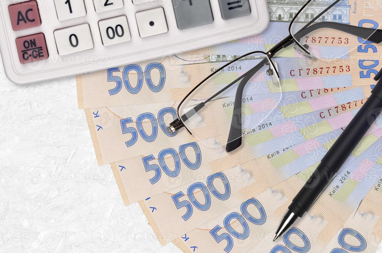 Ventilador de billetes de 500 hryvnias ucranianos y calculadora con gafas y bolígrafo. préstamo comercial o concepto de temporada de pago de impuestos foto