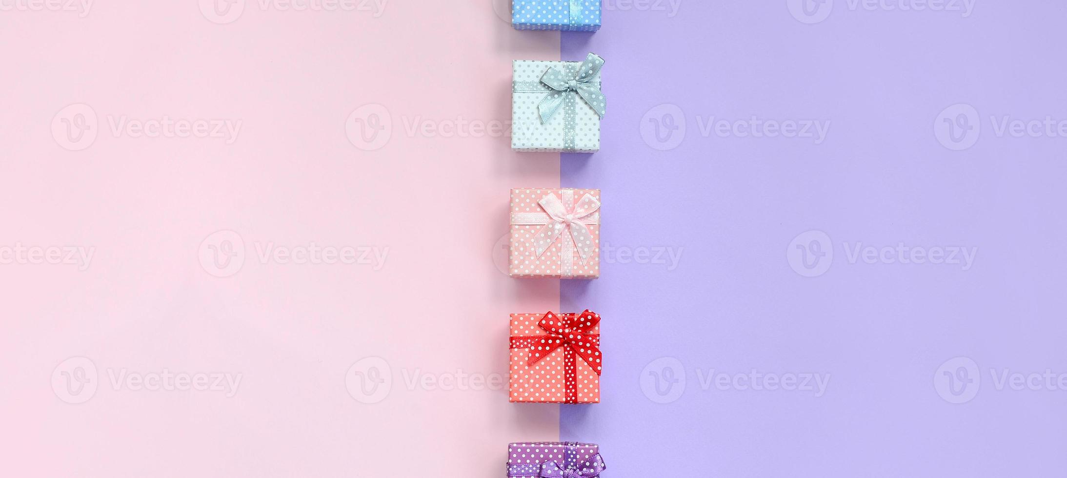 Small gift boxes of different colors with ribbons lies on a violet and pink color background photo