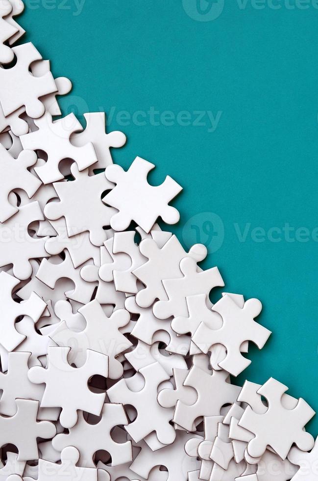 A pile of uncombed elements of a white jigsaw puzzle lies on the background of a blue surface. Texture photo with copy space for text