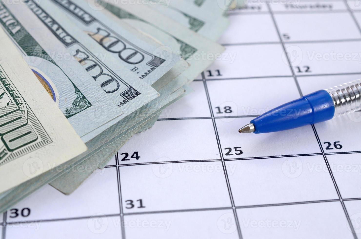 Pen and many hundred US dollar bills on calendar page close up photo