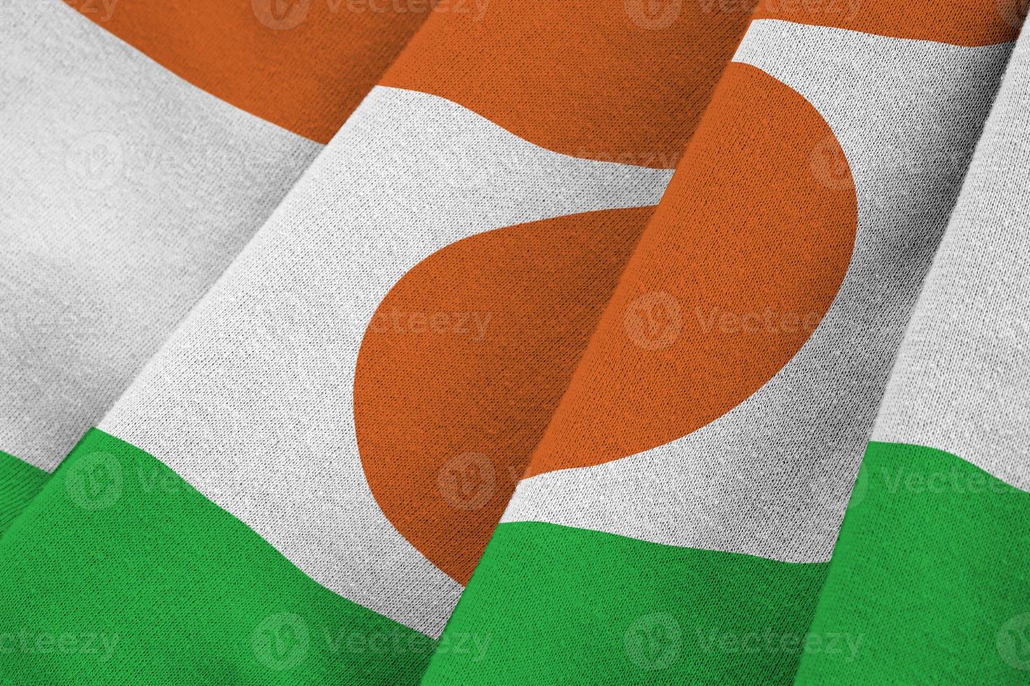 Niger flag with big folds waving close up under the studio light indoors. The official symbols and colors in banner photo