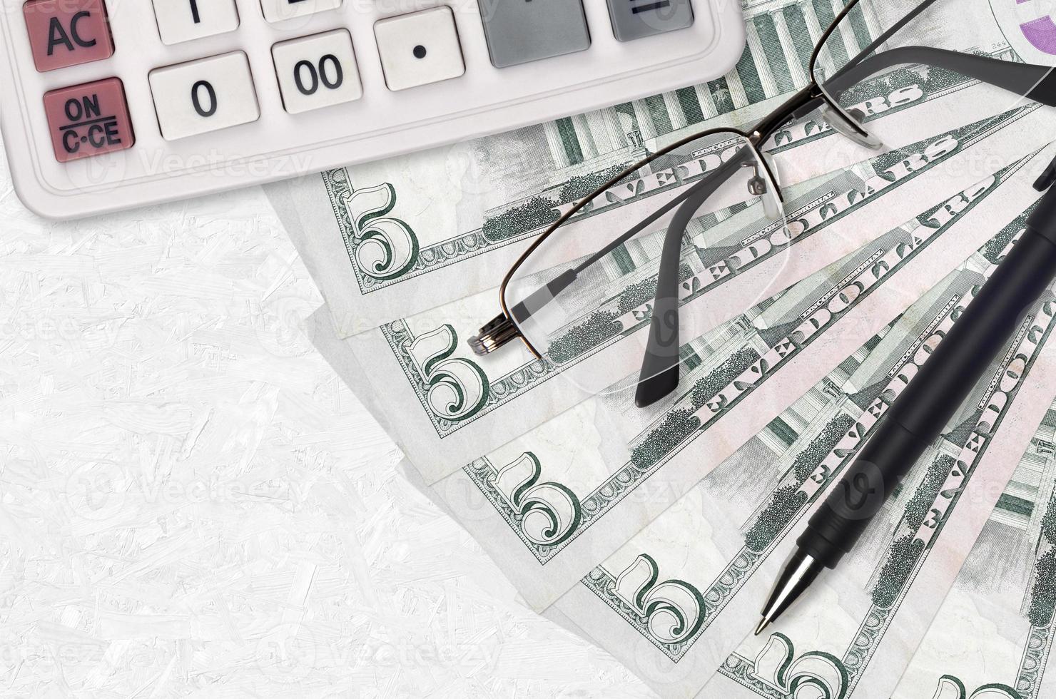 5 US dollars bills fan and calculator with glasses and pen. Business loan or tax payment season concept photo