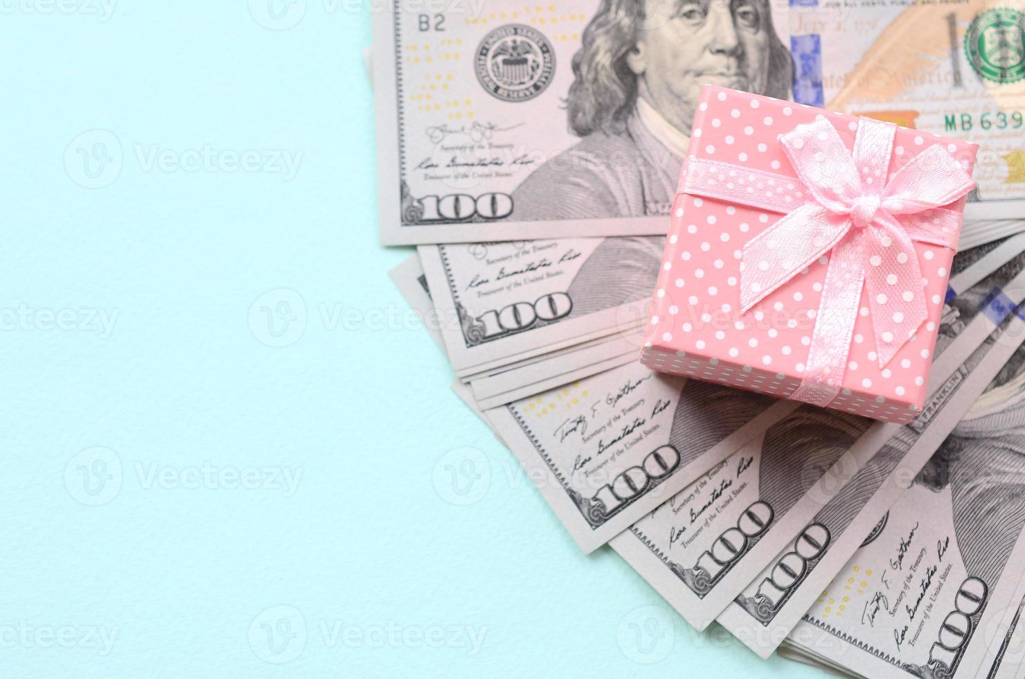 Pink dotted gift box lies near hundred dollar bills on a light blue background photo