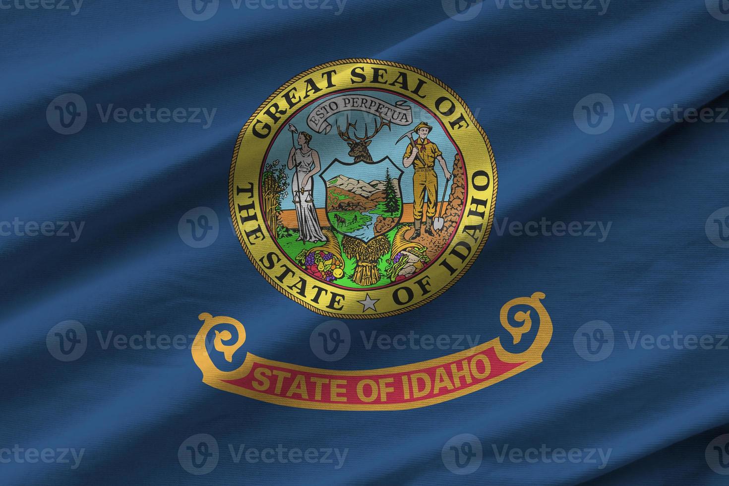 Idaho US state flag with big folds waving close up under the studio light indoors. The official symbols and colors in banner photo