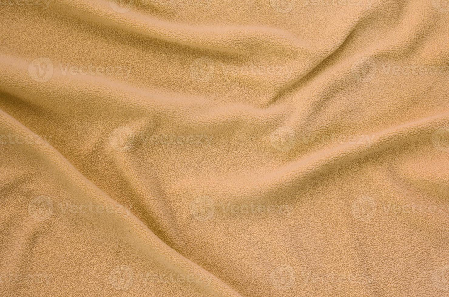 The blanket of furry orange fleece fabric. A background of light orange soft plush fleece material with a lot of relief folds photo