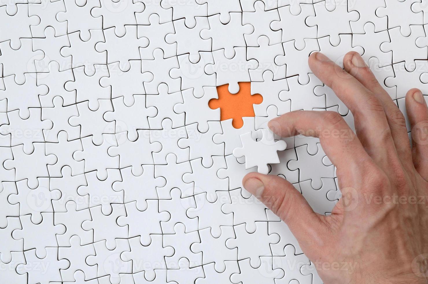 The texture of a white jigsaw puzzle in the assembled state with one missing element that the male hand puts in photo