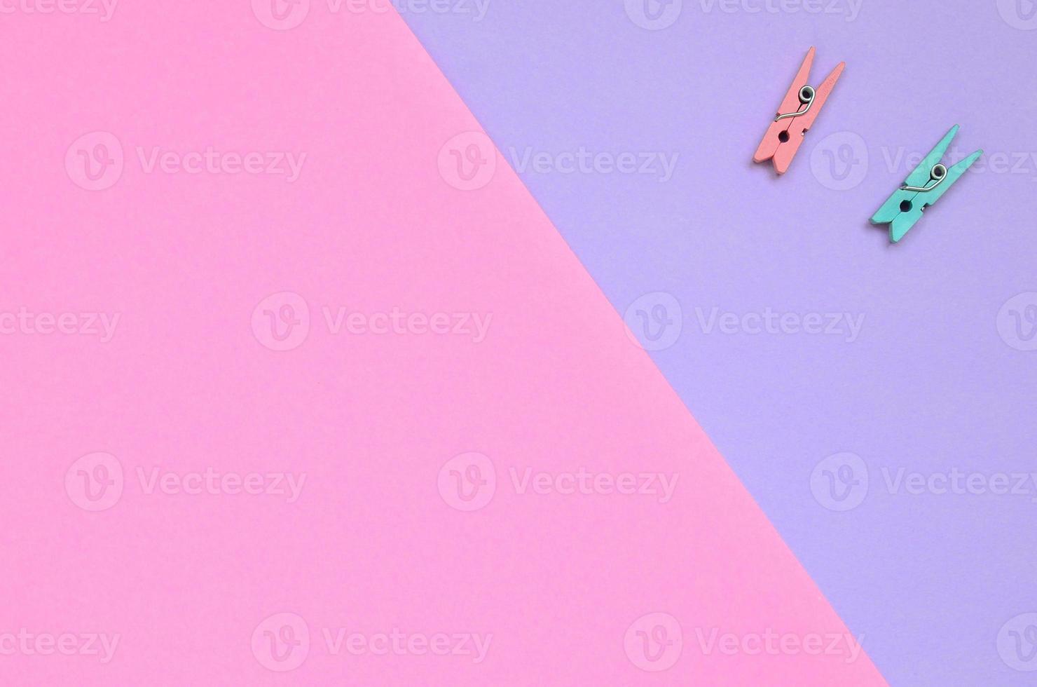 Two colored wooden pegs lie on texture background of fashion pastel violet and pink colors paper in minimal concept photo