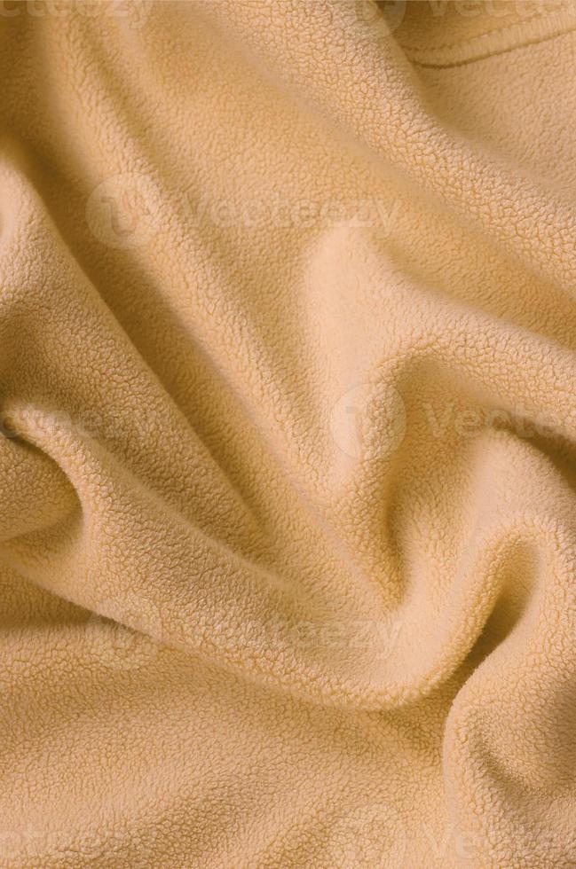 The blanket of furry orange fleece fabric. A background of light orange soft plush fleece material with a lot of relief folds photo