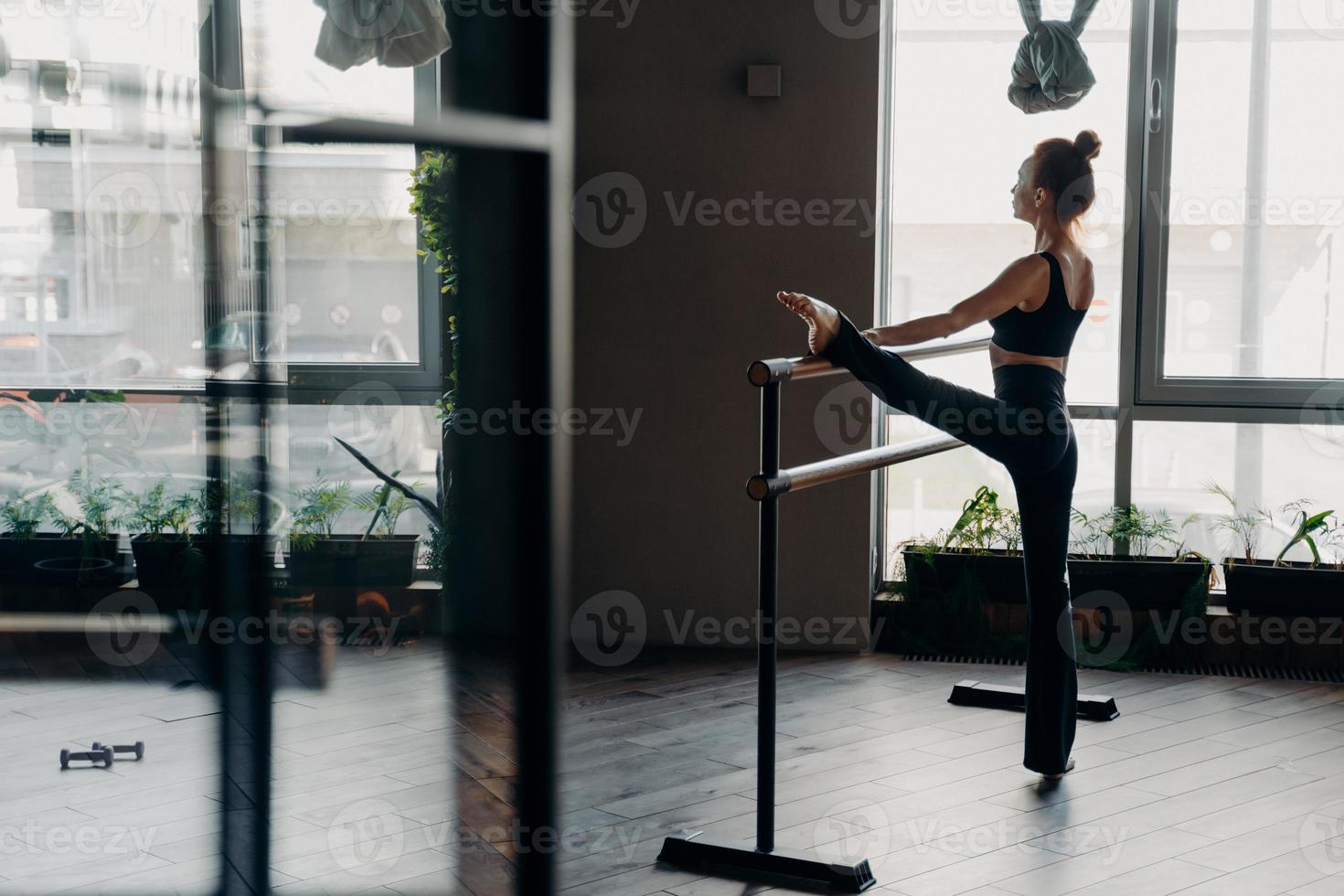 bailarina delgada durante su rutina de estiramiento a continuación en la barra de ballet en el estudio foto