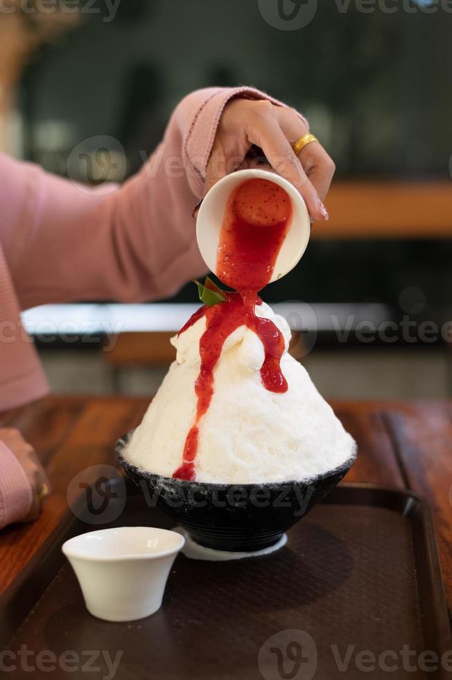 postre de hielo raspado coreano con coberturas dulces, bingsu de fresa en mesa de madera foto